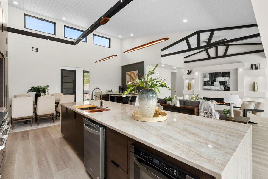 Kitchen with a center island with sink, light stone countertops, open floor plan, light wood finished floors, and a high ceiling
