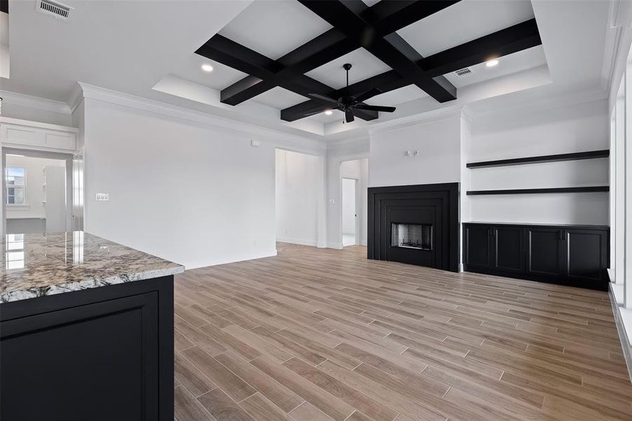 Unfurnished living room featuring beam ceiling, light hardwood / wood-style flooring, coffered ceiling, crown molding, and ceiling fan