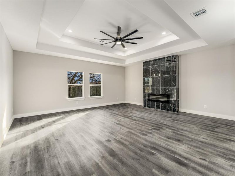 Unfurnished living room with hardwood / wood-style floors, a raised ceiling, ceiling fan, and a premium fireplace