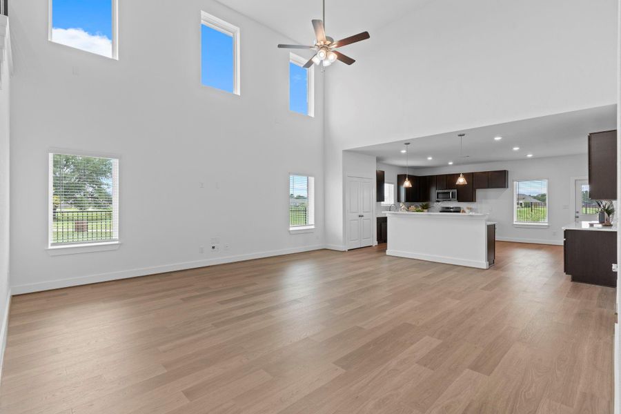 The open-concept family room is bathed in natural light from dramatic two-story windows, while woodlike vinyl floors and a ceiling fan add warmth and comfort—ideal for everyday living and entertaining. **Image Representative of Plan Only and May Vary as Built**. The open-concept family room is bathed in natural light from dramatic two-story windows, while woodlike vinyl floors and a ceiling fan add warmth and comfort—ideal for everyday living and entertaining. **Image Representative of Plan Only and May Vary as Built**.