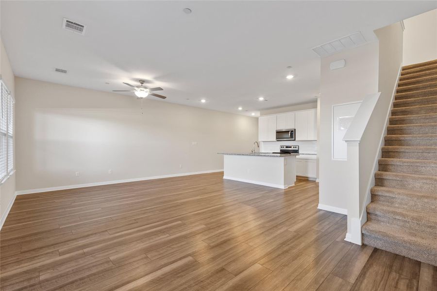 Unfurnished living room with light wood-style floors, recessed lighting, a ceiling fan, stairs, and healthy amount of natural light Unfurnished living room with light wood-style floors, recessed lighting, a ceiling fan, stairs, and healthy amount of natural light