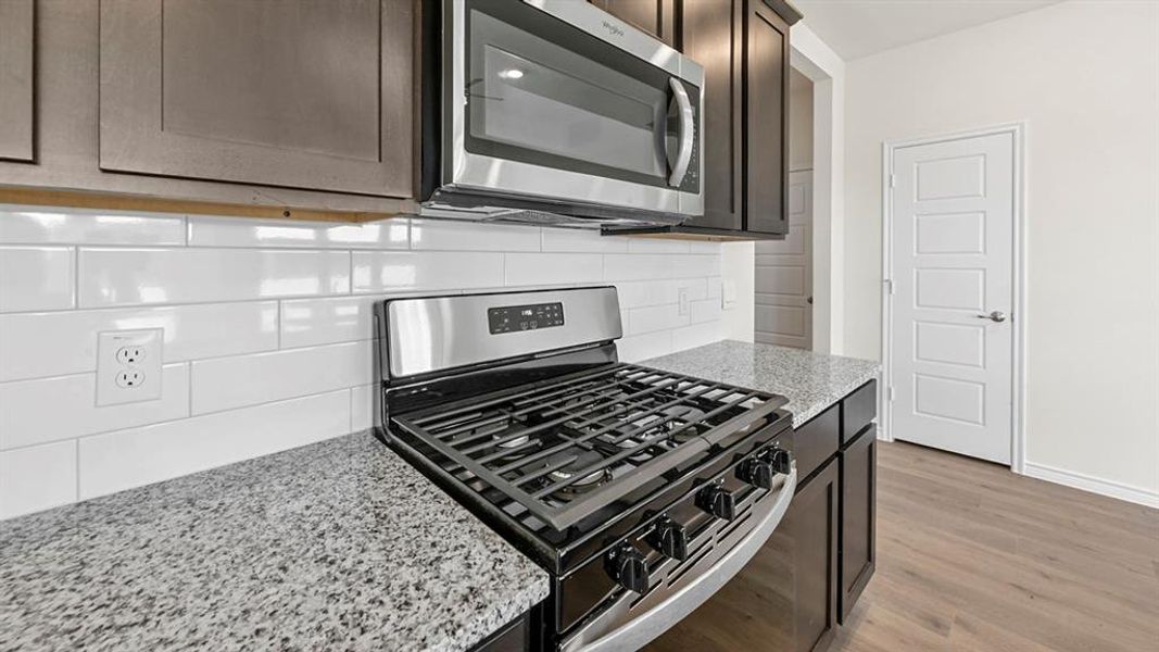 Kitchen with stainless steel appliances, light stone countertops, light wood finished floors, backsplash, and dark brown cabinetry