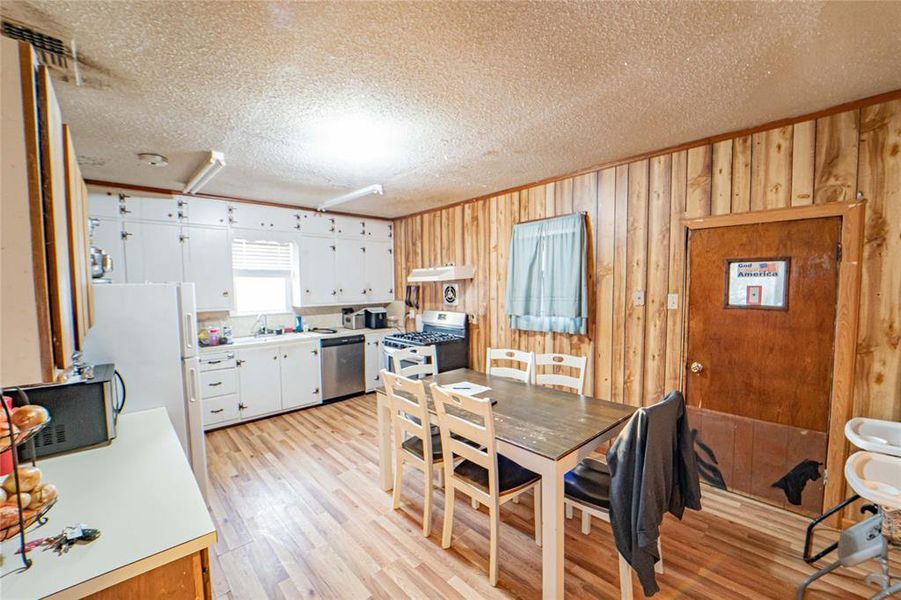 Dining area featuring a textured ceiling, wooden walls, light wood-style flooring, and ornamental molding Dining area featuring a textured ceiling, wooden walls, light wood-style flooring, and ornamental molding