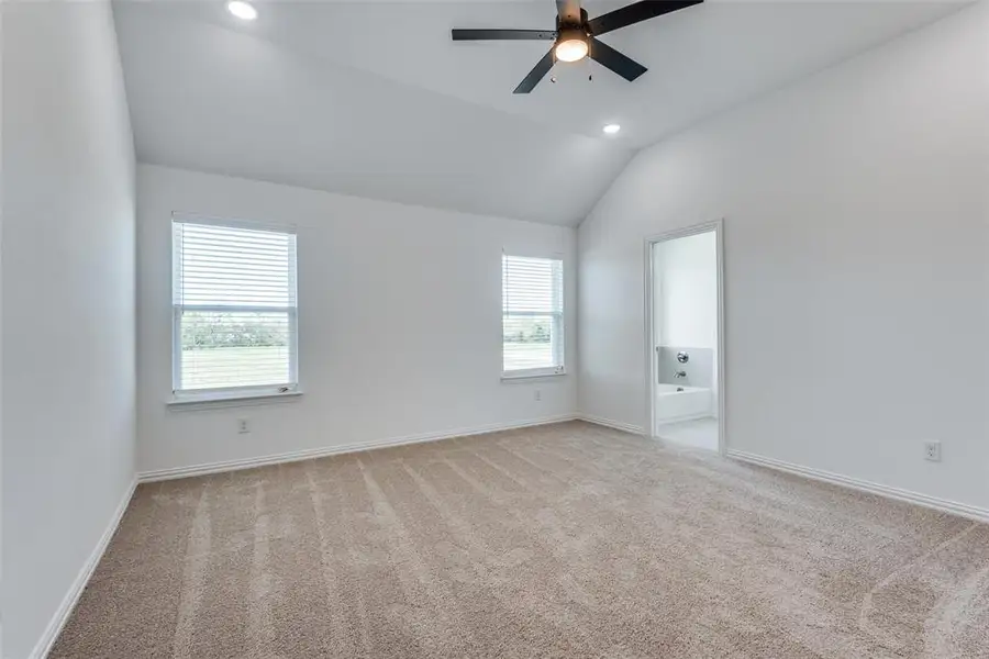 Spare room featuring light carpet, vaulted ceiling, and ceiling fan