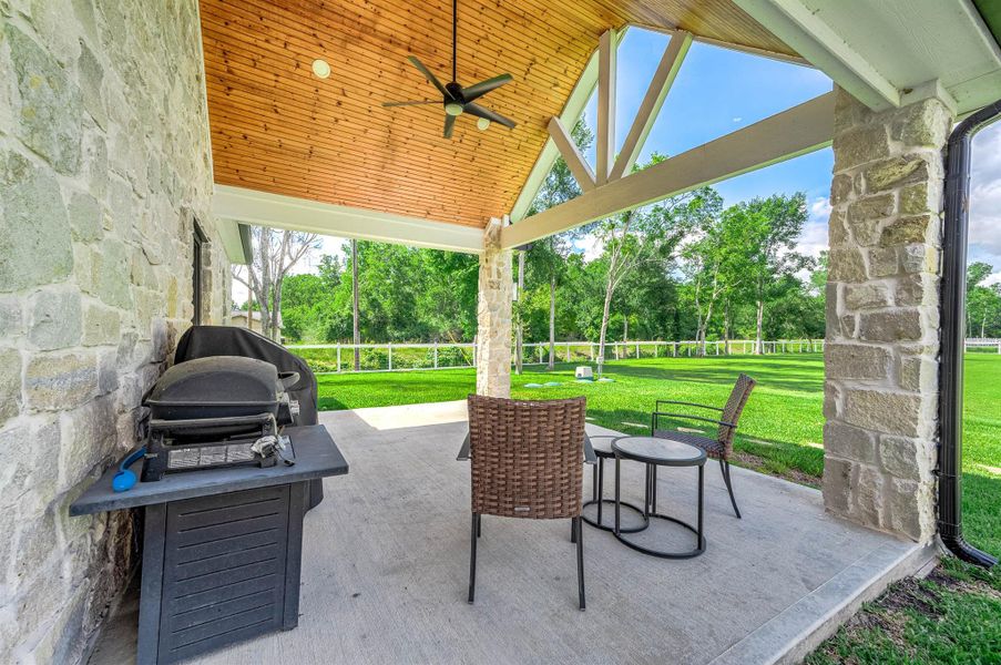 Enjoy outdoor living year-round on the covered back patio featuring a wood-accented ceiling, stone columns, and ceiling fan for added comfort. With plenty of room for seating and grilling, this space is perfect for relaxing or entertaining while overlooking the backyard.