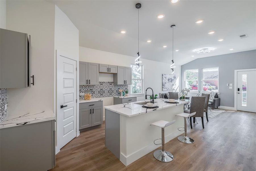 Kitchen featuring gray cabinets, vaulted ceiling, a kitchen island with sink, and sink