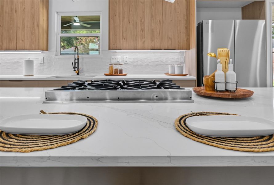 Sleek modern kitchen featuring a spacious marble island with built-in gas cooktop, complemented by warm wood cabinetry and stainless steel appliances.