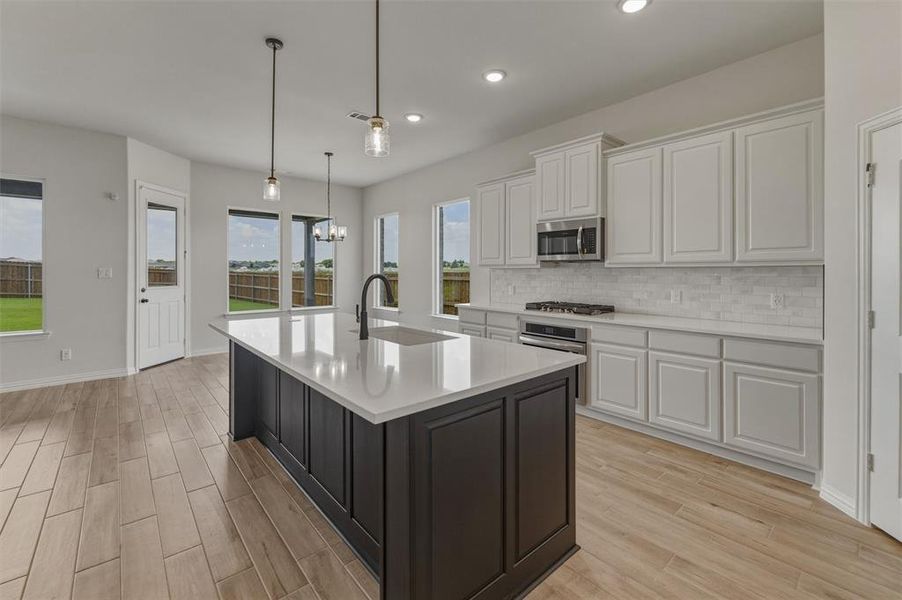 Contemporary kitchen featuring a dark-toned island with an integrated sink, light-toned perimeter cabinetry, stainless steel appliances, and wood-finish flooring Contemporary kitchen featuring a dark-toned island with an integrated sink, light-toned perimeter cabinetry, stainless steel appliances, and wood-finish flooring