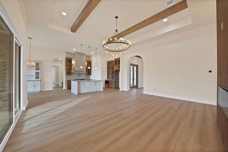 Unfurnished living room with arched walkways, recessed lighting, a chandelier, light wood-type flooring, and beamed ceiling Unfurnished living room with arched walkways, recessed lighting, a chandelier, light wood-type flooring, and beamed ceiling