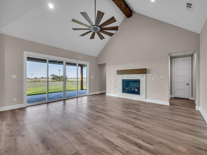 Unfurnished living room featuring beamed ceiling, high vaulted ceiling, light hardwood / wood-style floors, and ceiling fan