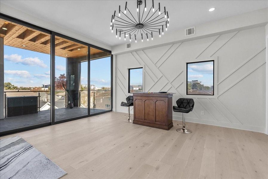 This modern space features large glass doors leading to a spacious balcony with great views. Inside, there's a stylish chandelier, light wood flooring, a chic accent wall, and a small bar area with stools, perfect for entertaining. This modern space features large glass doors leading to a spacious balcony with great views. Inside, there's a stylish chandelier, light wood flooring, a chic accent wall, and a small bar area with stools, perfect for entertaining.