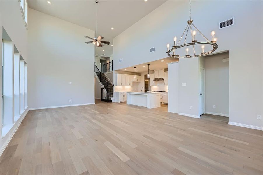 Living room featuring sink, light hardwood / wood-style floors, ceiling fan with notable chandelier, and high vaulted ceiling