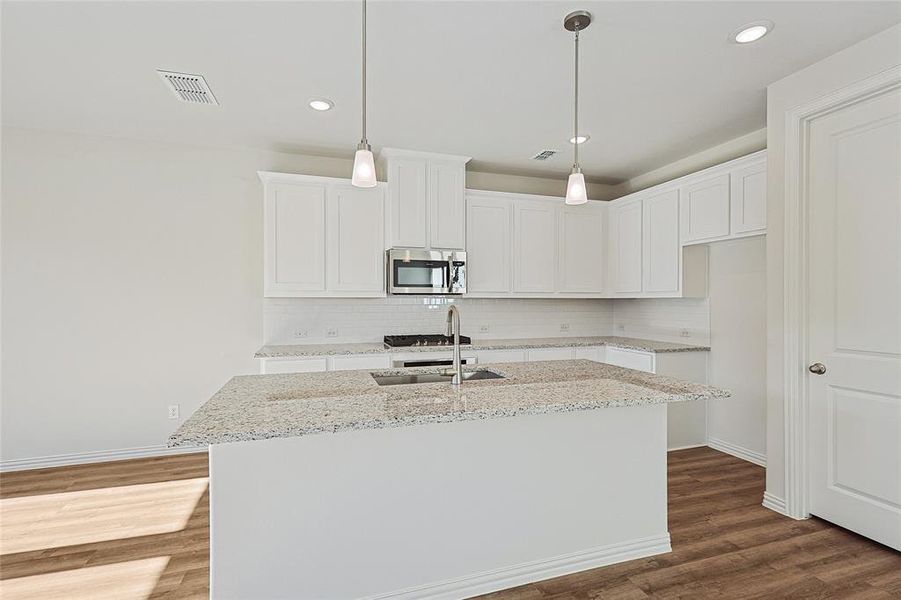 Kitchen featuring dark wood-type flooring, light stone countertops, a center island with sink, white cabinets, and stainless steel appliances