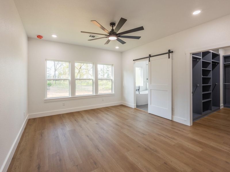 Wake up to peaceful views through triple windows in this spacious primary suite, complete with luxury vinyl plank flooring and a modern ceiling fan for added comfort. Wake up to peaceful views through triple windows in this spacious primary suite, complete with luxury vinyl plank flooring and a modern ceiling fan for added comfort.