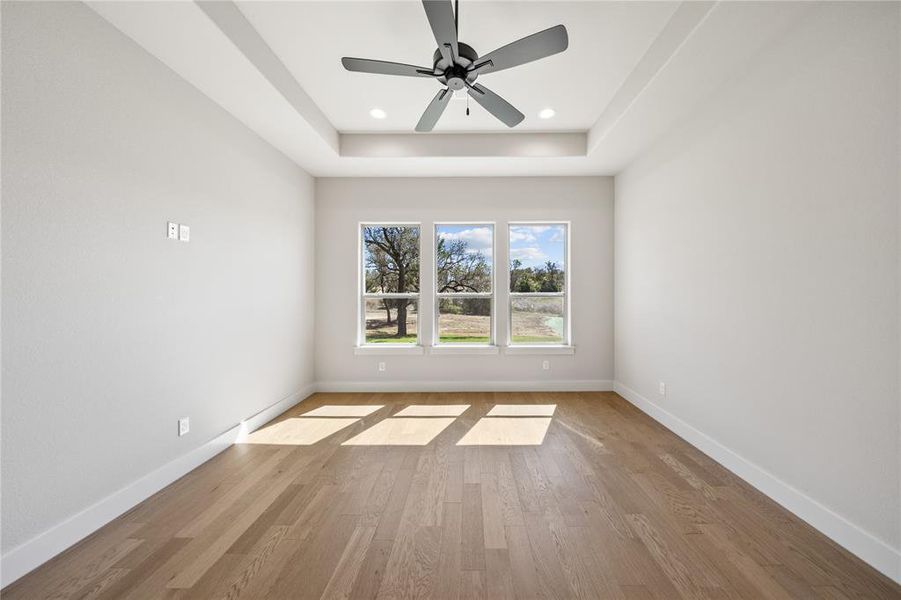 Empty room featuring a ceiling fan, light wood finished floors, recessed lighting, and a tray ceiling