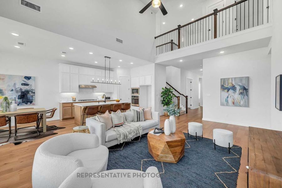 Living room featuring a high ceiling, light wood finished floors, recessed lighting, ceiling fan, and stairway Living room featuring a high ceiling, light wood finished floors, recessed lighting, ceiling fan, and stairway