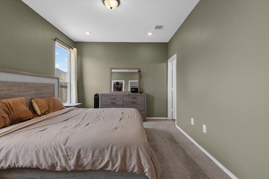 A restful bedroom offers comfort with plush carpeting and ample natural light through a tall window.