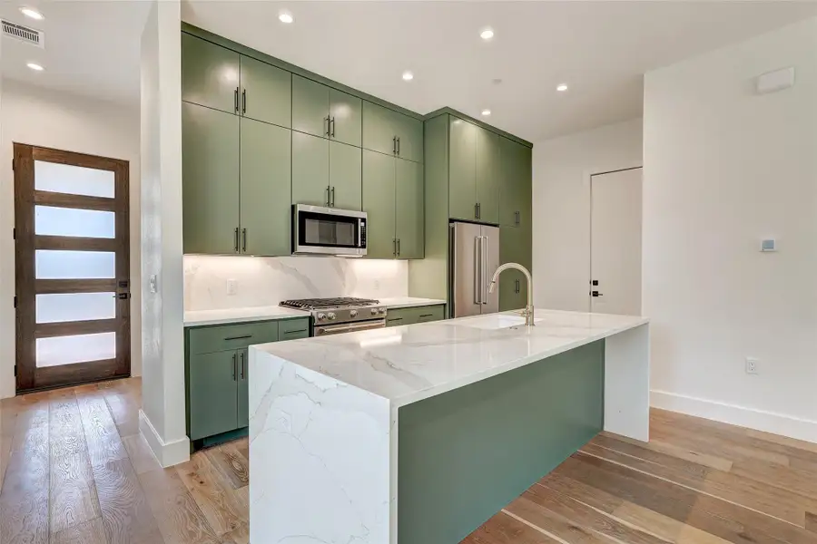 Kitchen with green cabinets, stainless steel appliances, light wood-style floors, a sink, and baseboards