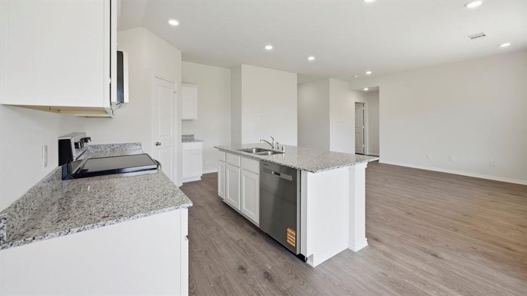 Kitchen featuring light stone countertops, light wood-type flooring, a kitchen island with sink, white cabinets, and recessed lighting