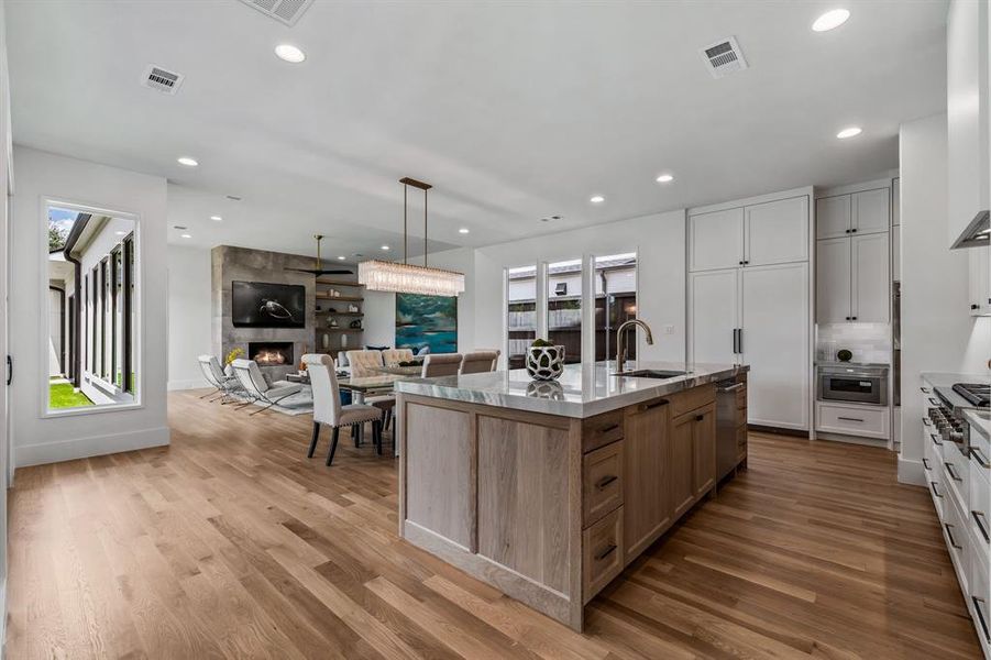 Kitchen featuring white cabinetry, a tile fireplace, a kitchen island with sink, and light wood-type flooring