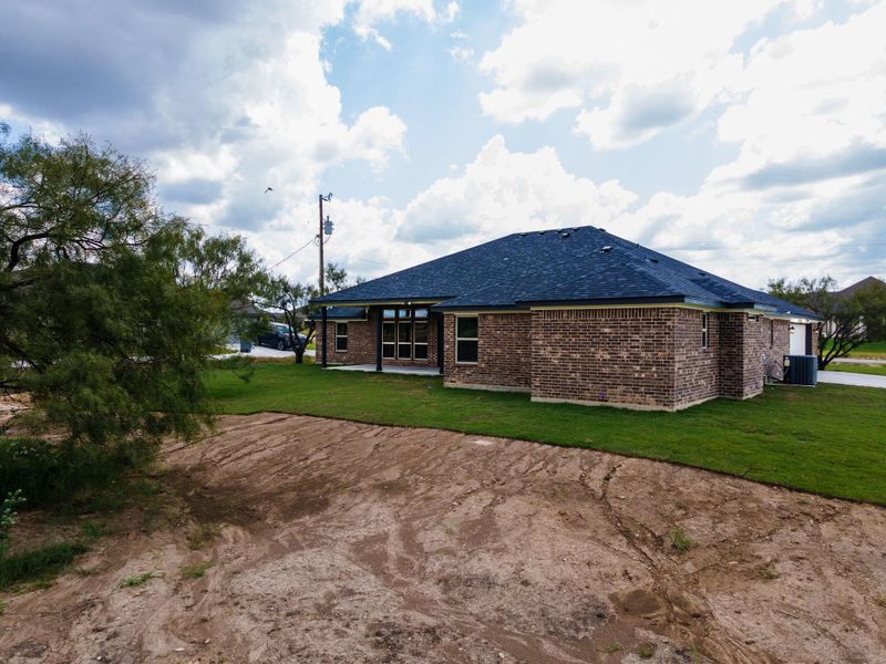 Back of property featuring a yard, a patio area, brick veneer, and roof with shingles Back of property featuring a yard, a patio area, brick veneer, and roof with shingles