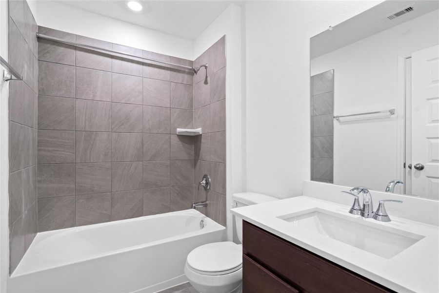 Secondary bath features tile flooring, tub/shower combo with tile surround, stained wood cabinets, beautiful light countertops, mirror, sleek fixtures and modern finishes.