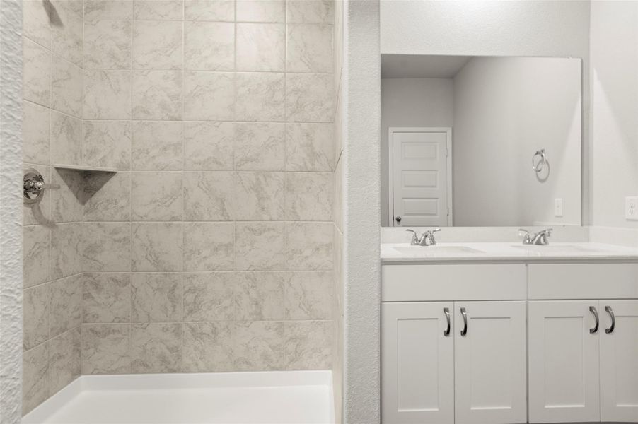 Full bath featuring double vanity and tiled shower