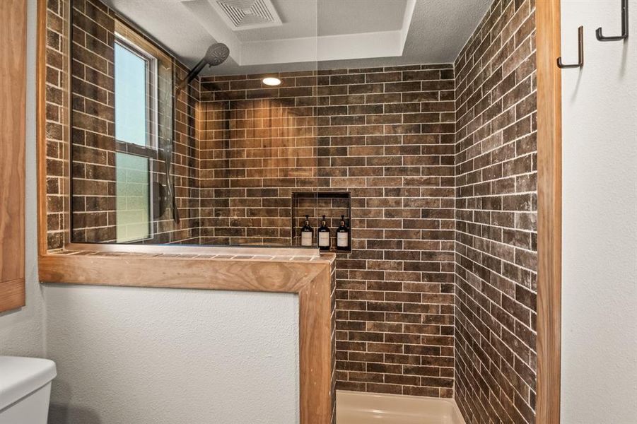Full bathroom with a stall shower, a raised ceiling, and brick wall