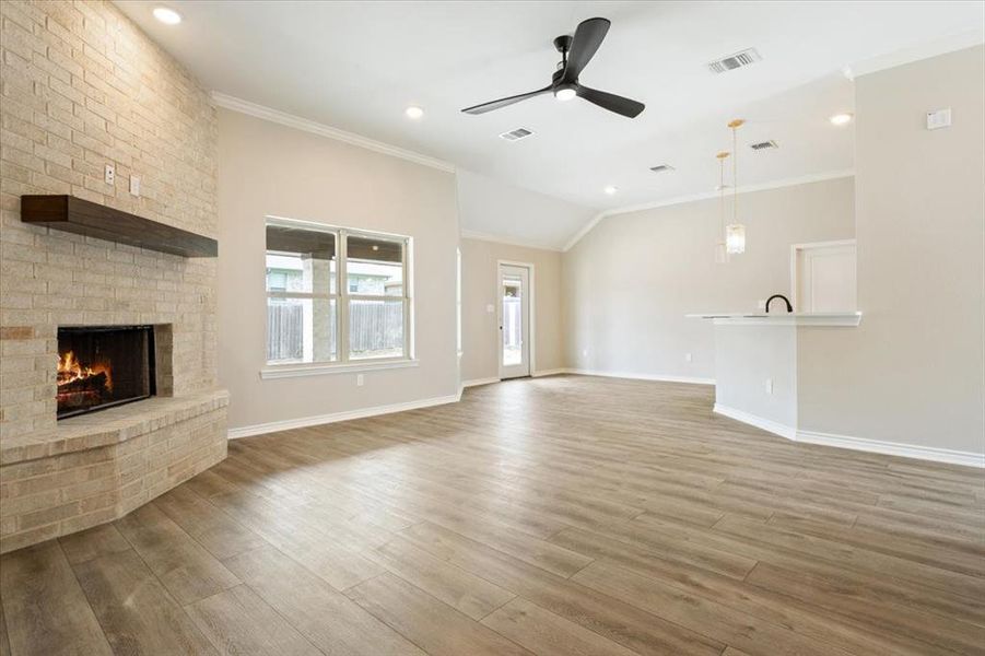Unfurnished living room with ceiling fan, wood finished floors, a fireplace, ornamental molding, and lofted ceiling Unfurnished living room with ceiling fan, wood finished floors, a fireplace, ornamental molding, and lofted ceiling