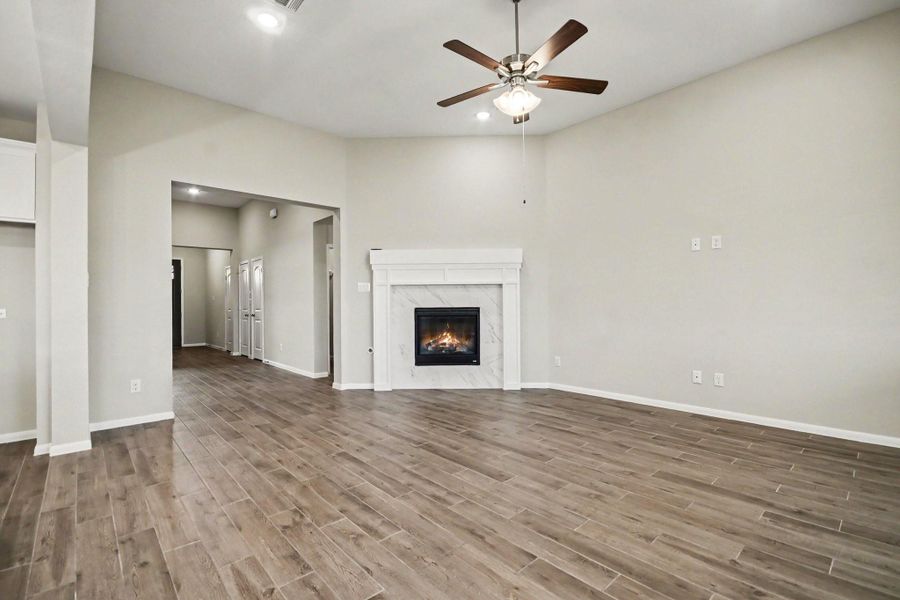 Spacious living area with elegant wood-look tile flooring, cozy fireplace, and ceiling fan, offering a warm and inviting atmosphere.
