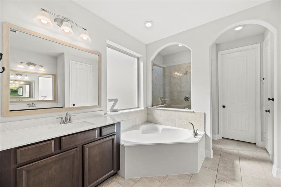 This restroom featuring a large vanity with dual sinks and framed mirrors, a soaking tub, a separate glass-enclosed shower, and a private toilet area. The room is finished with neutral colors and tiled flooring, offering a clean and bright space.