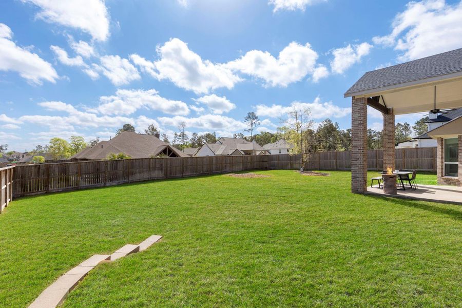 Spacious backyard with lush green lawn, a wooden fence for privacy, and a covered patio ideal for outdoor dining and relaxation. Perfect for family gatherings and enjoying sunny days.