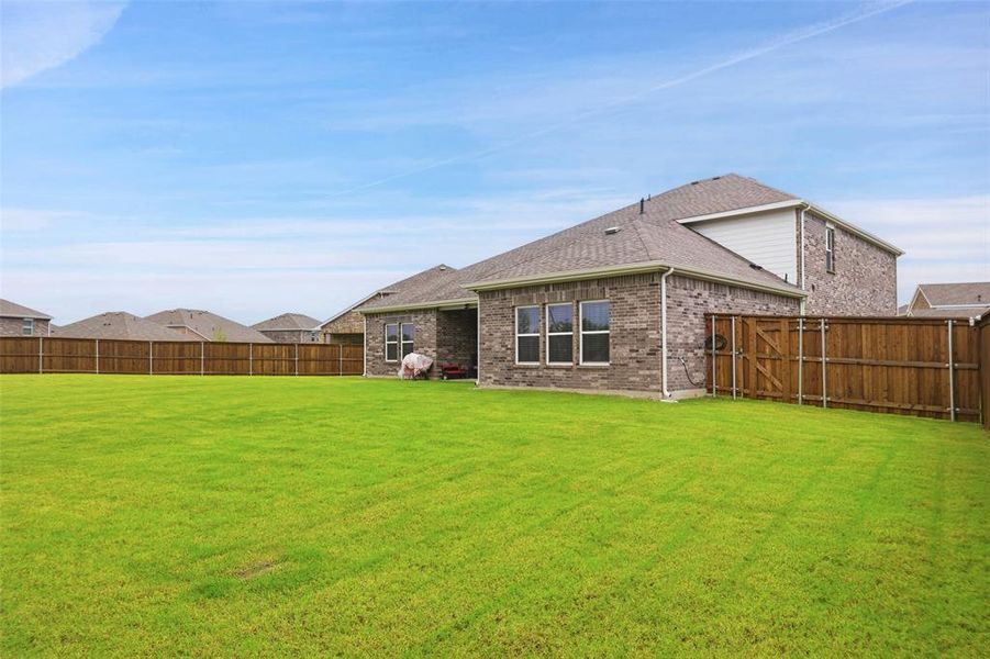 Expansive backyard featuring a lush green lawn, full wood-plank fencing, a two-story brick exterior, and multiple windows providing interior light