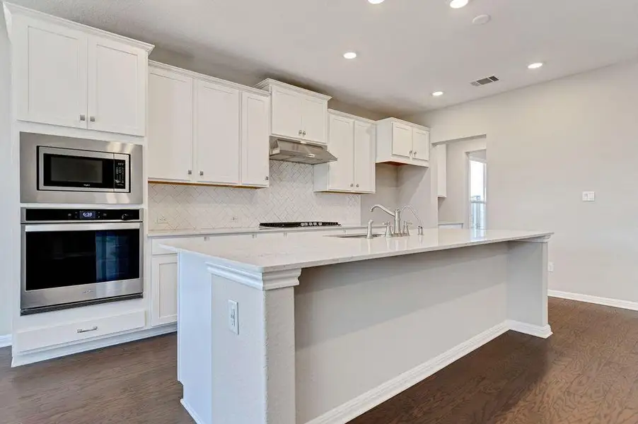 Kitchen with decorative backsplash, stainless steel appliances, dark wood-style flooring, light stone countertops, and white cabinets Kitchen with decorative backsplash, stainless steel appliances, dark wood-style flooring, light stone countertops, and white cabinets