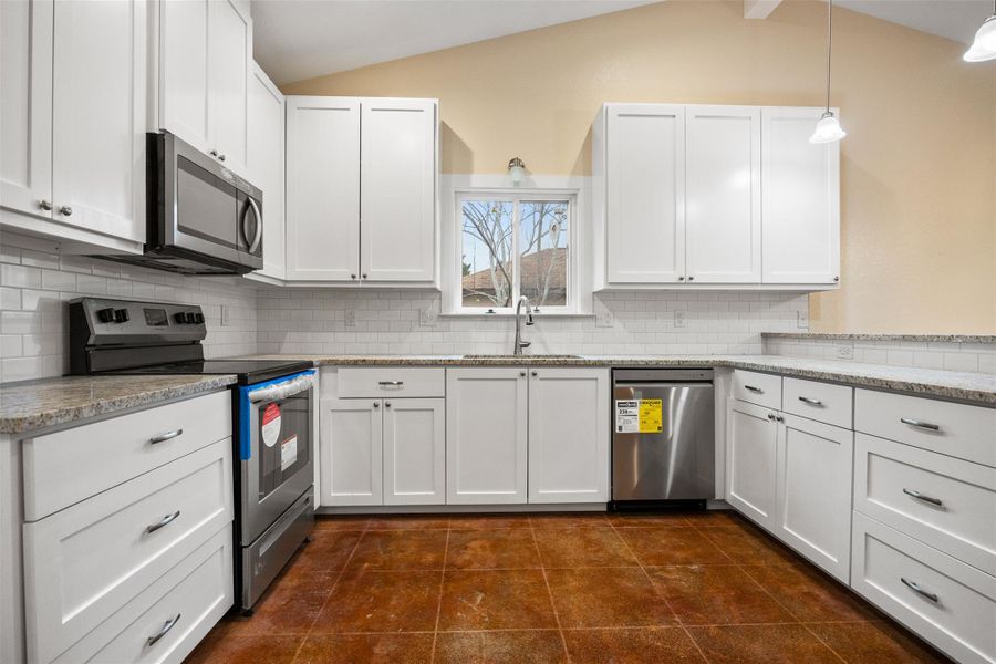Kitchen featuring appliances with stainless steel finishes, white cabinetry, tasteful backsplash, vaulted ceiling, and light granite countertops