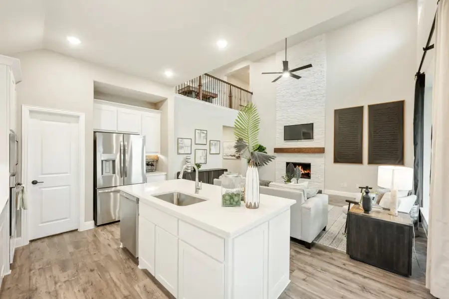 Open-concept kitchen and living area with white island, stainless appliances, stone fireplace, and second-floor loft overlook