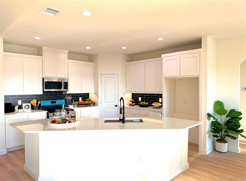 Kitchen featuring white cabinetry, decorative backsplash, an island with sink, light wood finished floors, and stainless steel appliances