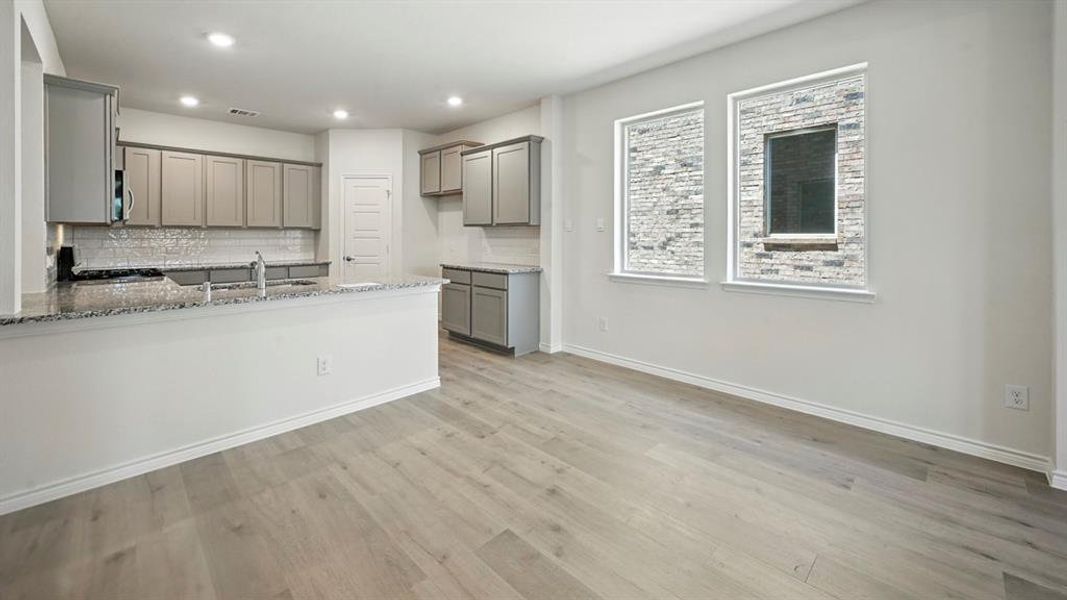 Kitchen with gray cabinets, backsplash, light stone counters, light wood-style floors, and a peninsula