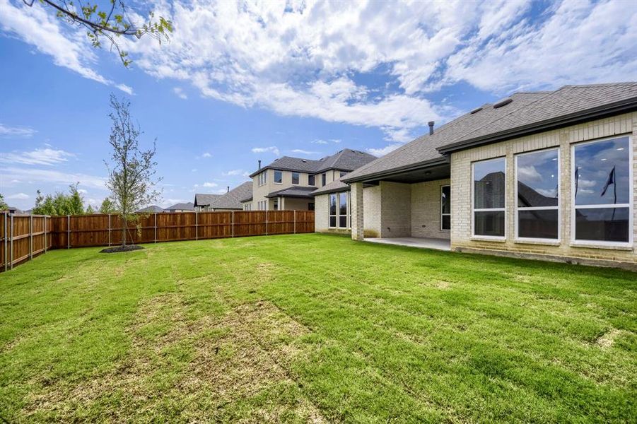 Expansive backyard featuring a manicured lawn, a full wood privacy fence, and a covered concrete patio