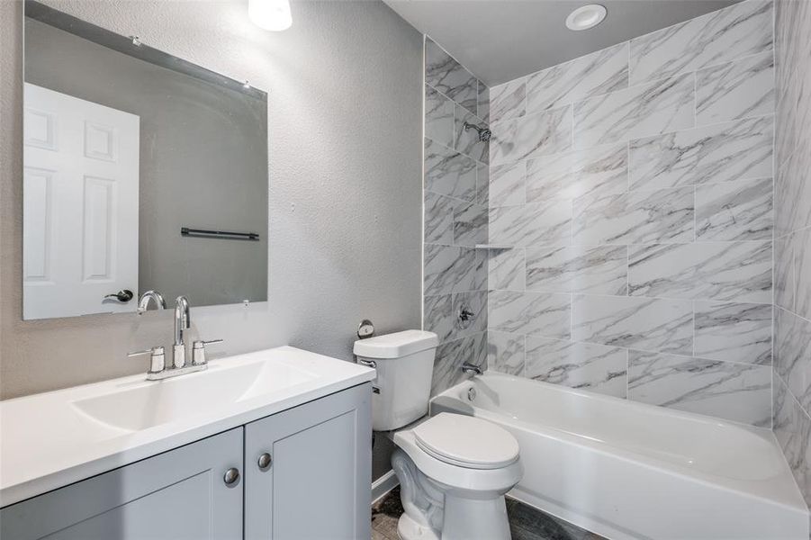 Full bathroom with toilet, tiled shower / bath combo, and vanity