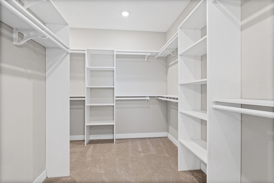 Spacious walk-in closet featuring white built-in shelving, multiple hanging rods, and recessed lighting Spacious walk-in closet featuring white built-in shelving, multiple hanging rods, and recessed lighting