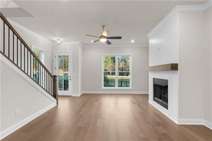 Unfurnished living room with stairs, light wood finished floors, plenty of natural light, ornamental molding, and a fireplace