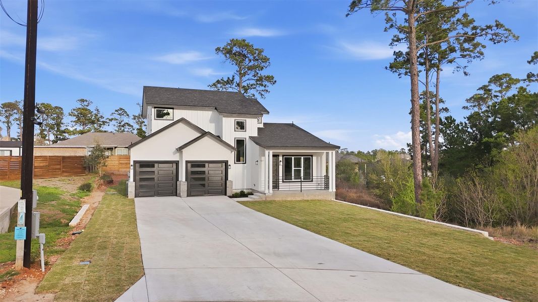 Modern farmhouse featuring concrete driveway, a shingled roof, a front lawn, and an attached garage