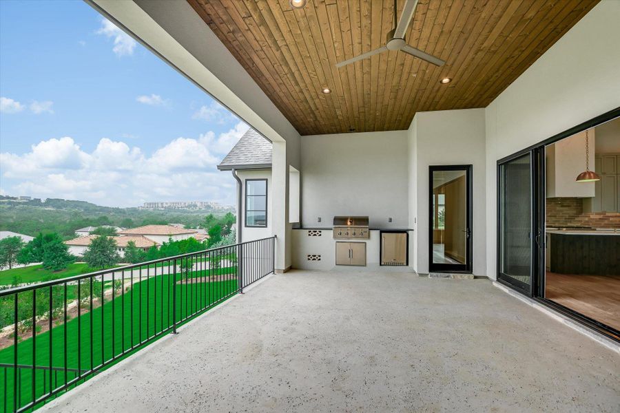 Expansive outdoor patio featuring an outdoor kitchen with grill and refrigerator, wood-finish ceiling with recessed lighting and ceiling fan, and sliding glass doors