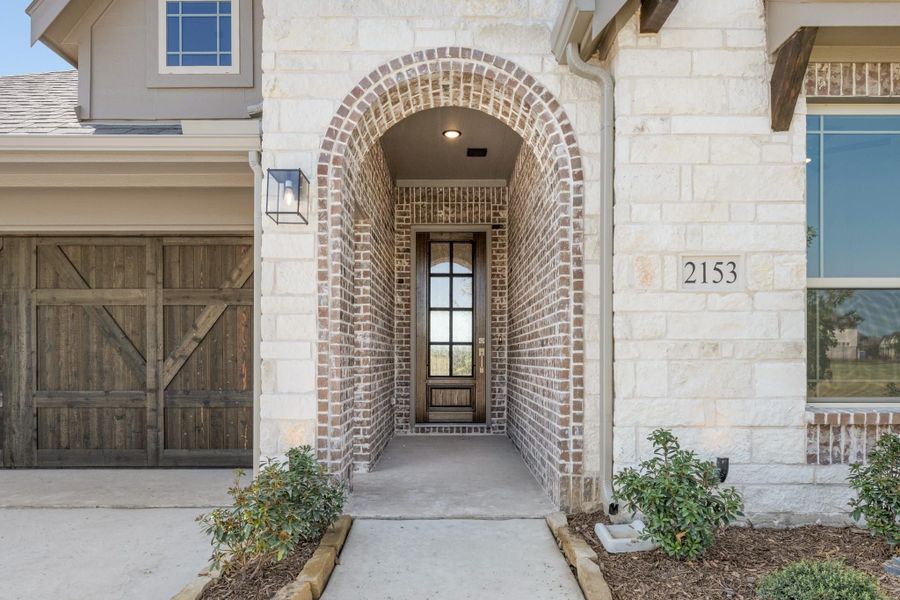 Home entrance with brick arched entryway, wood front door with glass panels, and rustic garage door beside it.