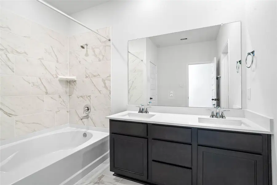 This spacious ensuite primary bathroom is move-in ready! With a dark stained vanity with light countertop and dual sinks, large mirror, tub/shower combination with tile surround, tile flooring, and sleek modern fixtures.