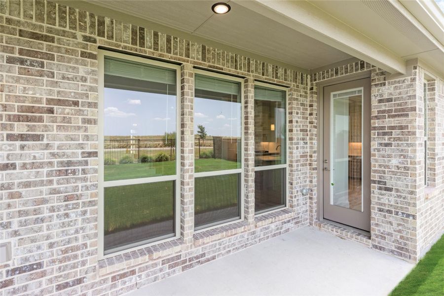 Covered back patio with brick exterior, large windows, and glass door overlooking fenced backyard