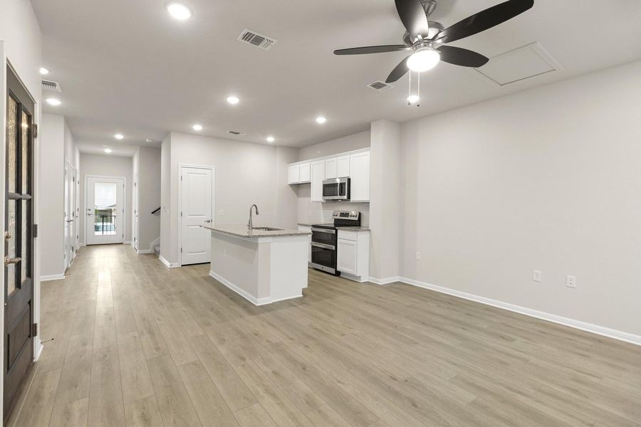 Open-concept living space with light-toned flooring, recessed lighting, and a ceiling fan
