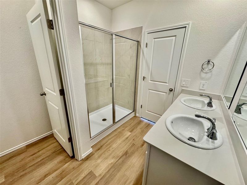 Bathroom featuring a textured wall, light wood-style flooring, a stall shower, and double vanity