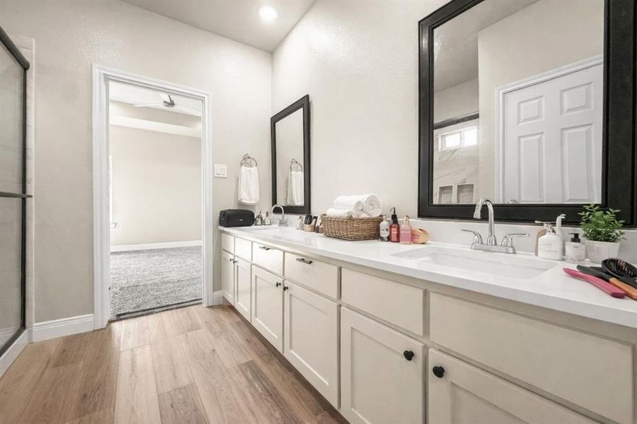 Bathroom with double vanity, light wood finished floors, and a stall shower